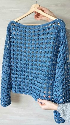 a blue crocheted sweater hanging on a wooden hanger next to a white wall