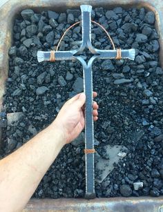 a person holding a metal cross in front of some rocks and gravel with their hand on it