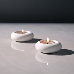 two white candles sitting on top of a table next to each other with one lit candle in the middle