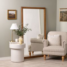 a living room with a chair, mirror and vase on the floor in front of it