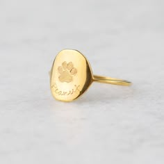 a gold ring with a dog's paw and name engraved on the front, sitting on a white surface