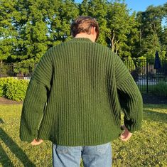 a man standing in the grass with his back to the camera, wearing a green sweater