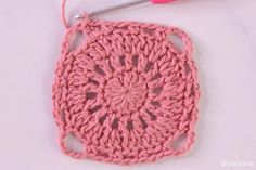 the crochet square is being worked on by a pink yarn ball and knitting needles