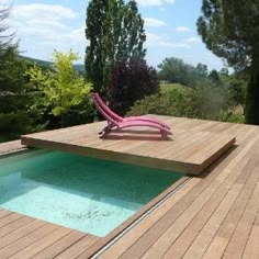 a pink chair sitting on top of a wooden deck next to a swimming pool in the middle of a forest