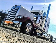 a large semi truck parked on top of a dirt field next to a boat trailer