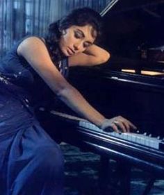 a woman in a blue dress leaning over a piano