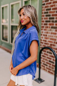 - This casual top is a trendy update to a timeless closet staple! - Lightweight material - A collared neckline - A button-up front - Short sleeves with rolled cuffs - Gathered detail at the shoulders and on the back - A relaxed silhouette that ends in a rounded hemline Blue Blouse With Button Closure And Collared Neckline, Chic Blue Top With Collared Neckline, Trendy Blue Collared Blouse, Blue Collared Blouse With Rolled Sleeves, Chic Blue Tops With Collared Neckline, Trendy Collared Blue Blouse, Trendy Blouse With Collared Neckline, Chic Blue Collared Blouse, Blue Collared Blouse For Work