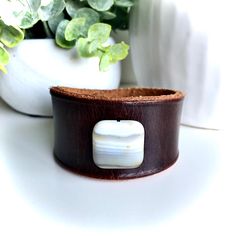 This handmade, brown leather cuff bracelet with white agate bead is made from high quality rawhide leather and features MishaGirl's signature design. It's a super cute leather accessory that goes well with a variety of styles. This also makes a great gift for women who love unique and interesting leather jewelry and accessories.  Fits wrist sizes 5 3/4 inches to 6 1/4 inches Inside Measurement 6 3/8 inches Width 1 1/2 inches at the widest part The leather cuff is dyed a dark brown color, which b Adjustable White Leather Bracelets, Brown Leather Cuff Jewelry, Adjustable White Leather Bracelet, Brown Rectangular Leather Jewelry, Brown Leather Rectangular Jewelry, Adjustable Brown Cuff Jewelry, Brown Leather Rectangular Bracelet, Brown Rectangular Leather Strap Bracelet, Adjustable Leather Rectangular Wristband