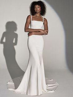 a woman in a white dress posing for the camera with her shadow on the wall behind her