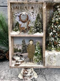 an altered christmas scene is displayed in a wooden box with snow and evergreens on the sides