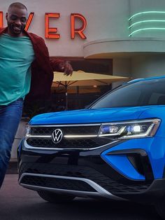 a man walking next to a blue volkswagen suv in front of a building with neon signs