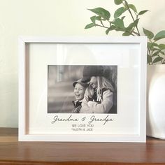 a photo frame with a couple holding each other on a table next to a potted plant