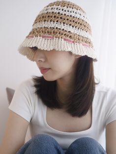 a woman sitting on the floor wearing a brown and white crocheted hat with fringes