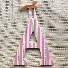 a pink and green striped wooden letter hanging from a string on top of a bed