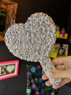 a person holding up a heart shaped brooch with lots of crystals on top of it