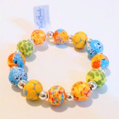 a bracelet with colorful beads and charms on it's side, sitting on a white surface