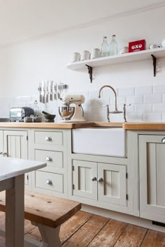 a kitchen with wooden floors and white cabinets, an island table and shelves above the sink