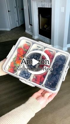 a person holding a plastic container filled with berries and strawberries in front of a fireplace