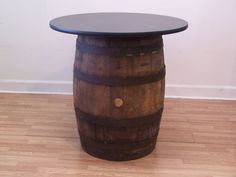 a wooden barrel table sitting on top of a hard wood floor next to a white wall