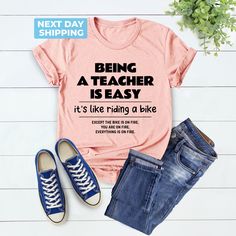 Cute Teacher Shirt, Being A Teacher Is Easy Back To School Like Riding A Bike, School Shirt, Funny Teacher Shirt, Unique Gift, Teacher Gift Hi! Welcome to the LaTeeApparel!  It's great to see you here! Our shirts are clean, high quality and soft. It is prepared quickly by our store! Enjoy your shopping! It is a pleasure for us to help you with your questions and you can reach us at any time. F I T  ∙ S I Z I N G  -->Women's sizes are narrower than the waist -->Sleeves are rolled up in some produ Casual Cotton T-shirt For Cycling, Short Sleeve Graphic Print Cycling Tops, Graphic Print Short Sleeve Cycling Top, Graphic Print Short Sleeve Tops For Cycling, Sped Teacher Shirts, Teacher Tshirt Ideas, Preschool Teacher Shirts, Sped Teacher, Riding A Bike