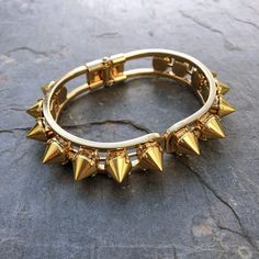 This stunning cuff is made of individually handset gold spikes in pronged settings, arranged around a hinge closure cuff. The oval shape fits comfortably on most wrists and is perfect for stacking or wearing solo. With its edgy design, this cuff will add a touch of rebellious glamour to any outfit. Whether you're dressing up for a night out or adding a little edge to your everyday look, the Helios Cuff is the perfect accessory for any occasion. DETAILS Bracelet Diameter: 7” Edgy Elegance, Cuffing Season, Metal Spikes, Edgy Design, Gold Rings Jewelry, Gothic Jewelry, Rings Jewelry, Monster High, Oval Shape