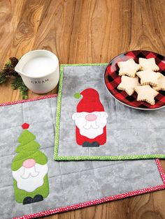 two placemats with santa claus and snowflakes on them next to a bowl of cookies