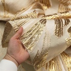 a hand is holding something that looks like gold foil on white fabric with black and gold stripes