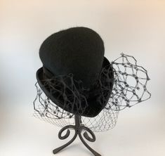 Elegant and whimsical, Makshy's heart shaped cocktail hat adds a touch of sophistication and flair to your formal event attire. Expertly crafted from high-quality wool felt and enriched by a sumptuous silk lining, this refined hat is an indispensable addition for women seeking to enhance their wardrobe with grace. Ideal for various events, including opulent parties, museum visits, or theatrical performances, this captivating vintage hat makes a memorable impression. The distinctive heart shape and delicate veil suit brides, mothers of the bride or groom, and fashion enthusiasts. This versatile fascinator is perfect for cocktail events, charity functions, and social gatherings, with its durable construction ensuring lasting elegance and charm. FEATURES * Expertly crafted and handmade in Gre Handmade Fitted Vintage Fascinator, Handmade Formal Hats, Winter Party Top Hat With Curved Brim, Adjustable Brimmed Felt Hat For Evening, Fitted Hats For Halloween Evening, Elegant Adjustable Mini Hats For Halloween, Elegant Fitted Hat For Halloween, Fitted Winter Evening Fascinator, Elegant Halloween Fascinator