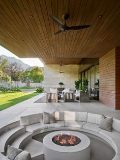 a fire pit sitting on top of a patio next to a lush green field under a wooden roof