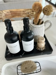 two bottles of soap sitting on top of a black tray next to a cup and brush