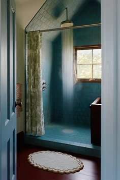 a blue tiled bathroom with a shower and rug on the floor in front of it