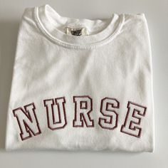 My absolute favorite tee! This 'NURSE' tee can be customized to your preferred thread color and is stitched on a Comfort Colors short sleeve unisex tee.  Please wash on gentle cycle and dry on low.  If you are wanting a different design, wording, or a different clothing style, please send me a message so we can discuss the details. Please include thread color at checkout If you need this order rushed, please add these to your cart: https://www.etsy.com/listing/1043569716/rush-my-order-for-t-shir College Crew Neck T-shirt With Letter Print, White Embroidered T-shirt For College, Embroidered Cotton Crew T-shirt, College Crew Neck T-shirt With Embroidered Logo, Crew Neck Top With Embroidered Logo For College, Crew Neck T-shirt With Letter Embroidery For College, Collegiate Embroidered Crew Neck T-shirts, White Relaxed Fit T-shirt With Letter Embroidery, Collegiate Cotton T-shirt With Embroidered Graphics