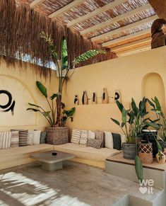 a living room filled with lots of furniture under a thatch roof covered in plants