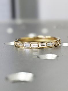 a gold wedding band with baguettes and diamonds on the side, sitting on a table