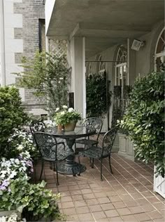 an outdoor dining area with potted plants on the porch and table in the foreground