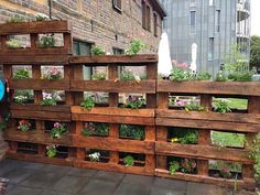 several wooden pallets filled with plants and flowers on the side of a brick building