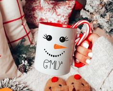 a person holding a coffee mug with a snowman face on it next to christmas decorations