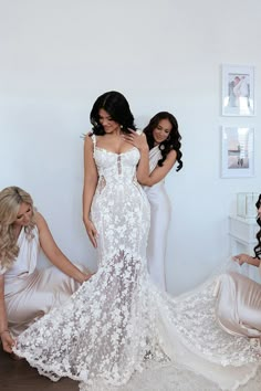 three beautiful women in white dresses posing for the camera with one woman looking at her dress