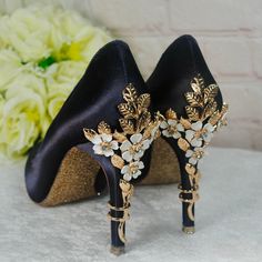 a pair of black high heeled shoes with gold and white flowers on the heels