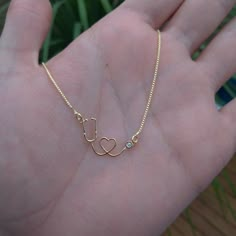 a hand holding a gold necklace with a heart and a stethoscope on it