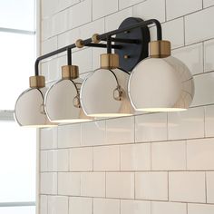 a bathroom light fixture with four lights on the wall and white tiled walls behind it