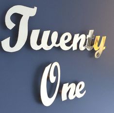 the word'twenty one'is cut out of white acrylic letters on a blue wall