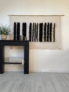 a wall hanging with black and white decorations on it next to a wooden table in front of a potted plant