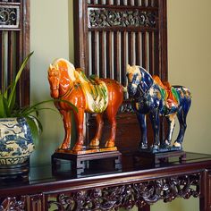 three ceramic horses are sitting on top of a table next to a potted plant