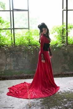 a woman in a long red dress is standing by an open window and looking at the camera