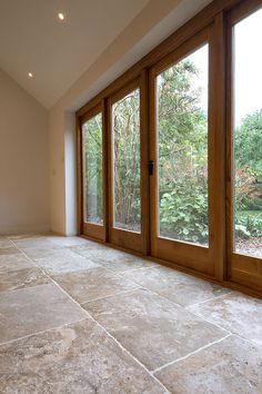 an empty room with large windows and stone flooring on the outside, looking out onto a wooded area