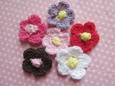 four crocheted flowers sitting on top of a pink table covered in polka dots