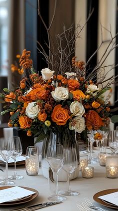 an arrangement of flowers in a vase on top of a table with candles and place settings