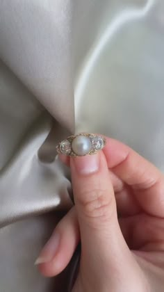 a woman's hand holding a pearl and diamond ring on top of a white cloth