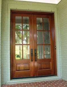 the front door is made of wood and has two glass panels on each side, along with brick flooring